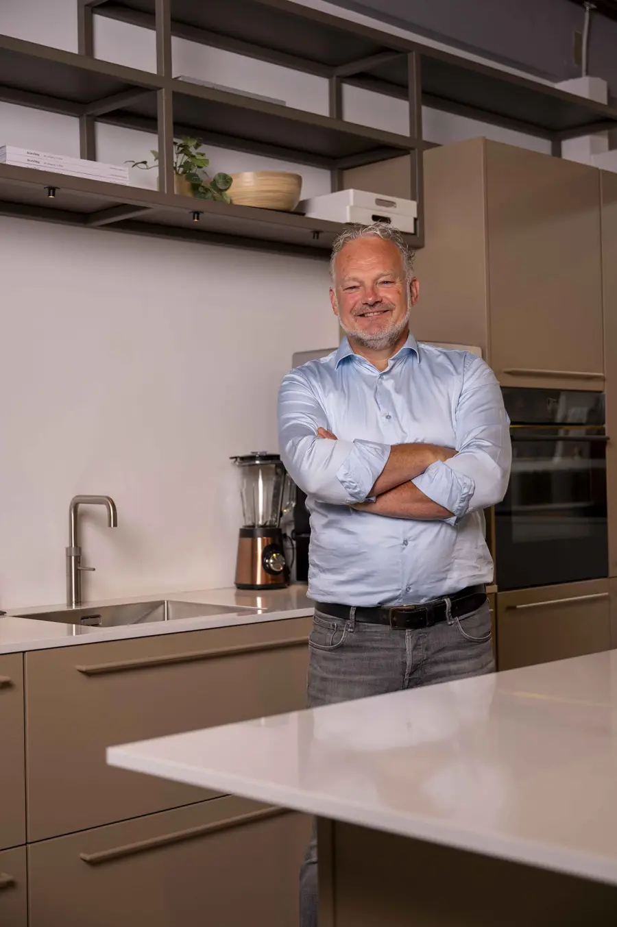 Henk van Veen staat lachend met zijn armen over elkaar in een stalen keuken