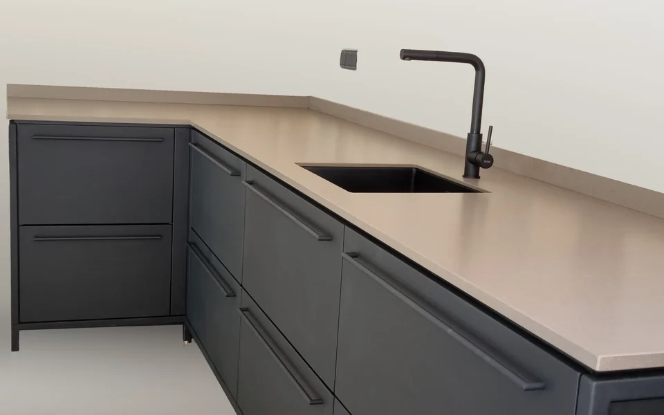 Buitenkeuken van Staal Staat met antraciet fronten, een taupe werkblad en een zwarte kraan tegen een stenen wand