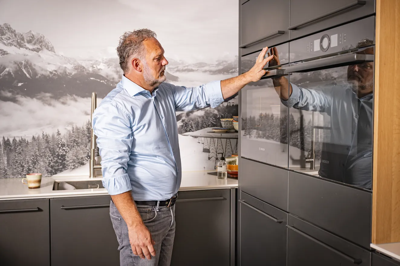 Henk van Veen bedient een inbouwoven in een zwarte stalen keuken